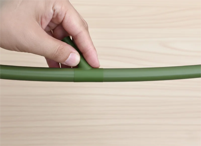 Zbliżenie ręki trzymającej zielony łącznik wyrównujący bambusowe elementy na drewnianej powierzchni.