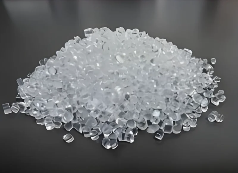 Груда прозрачных пластиковых гранул, разбросанных по темной поверхности, используемых в качестве сырья для производства.