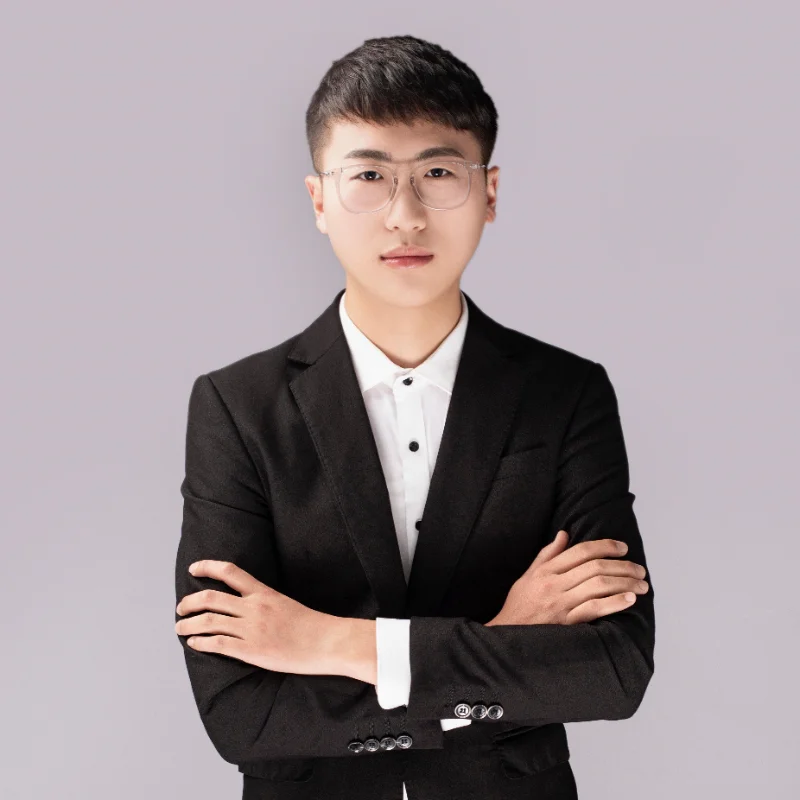 A man in a black suit and white shirt standing with arms crossed against a light gray background.