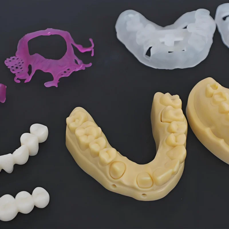 Various dental molds in different materials and colors displayed on a dark surface, showcasing prototype designs.