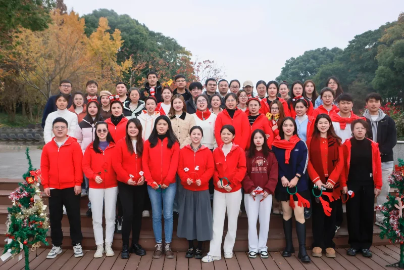 A group of people in red outfits standing outdoors on wooden steps, surrounded by trees and festive decorations.