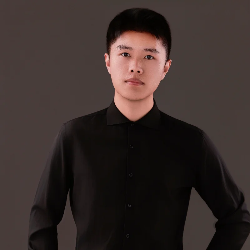 Individual in a black button-up shirt with blurred face, against a dark background.