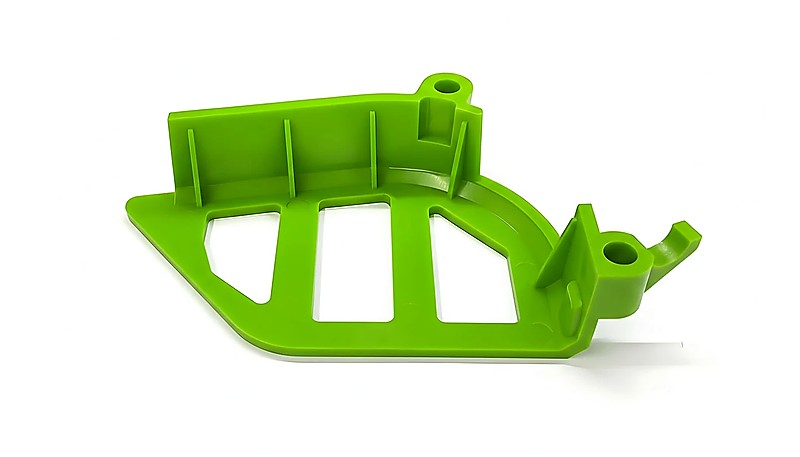 Green plastic injection molded part with a unique design and open spaces, showcasing intricate engineering.