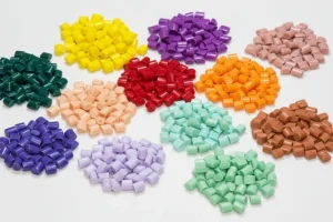 Various colored plastic pellets arranged in piles on a white surface, used for injection molding processes.