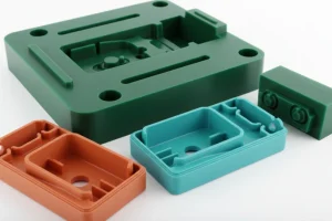 Green, brown, and blue plastic injection molds of different shapes on a white background.