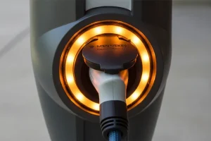 Close-up of an electric vehicle charging port with a plugged-in cable and glowing circular lights indicating charging status.