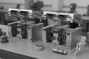 Two open metal injection molds displayed on a workshop table with various parts around them.