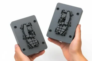 Hands holding two intricate plastic injection molds designed for precision manufacturing.